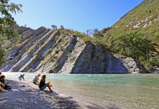 Familier nyder solskin ved floden med stejle klippeformationer i baggrunden, Huttopia Gorges du Verdon.