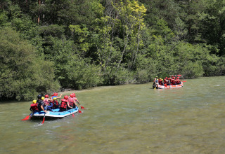 Folk i redningsveste og hjelme nyder rafting på en flod i det grønne område ved Huttopia Gorges du Verdon.