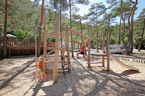 Niños juegan en un parque infantil de madera en Huttopia Gorges du Verdon, rodeados de naturaleza en Francia.