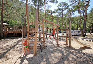 Børn leger på en legeplads omgivet af træer på Huttopia Gorges du Verdon feriepark i Frankrig.