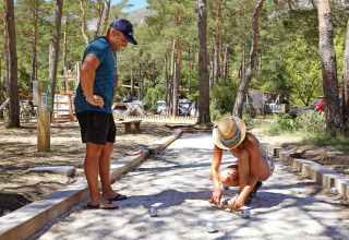 To personer spiller petanque på en grusbane omgivet af træer ved Huttopia Gorges du Verdon feriepark.