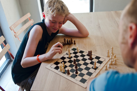 Een jongen speelt schaak met een volwassene aan een houten tafel bij Huttopia Gorges du Verdon, Hauts-de-France.