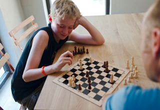 A boy plays chess with an adult at a wooden table in Huttopia Gorges du Verdon, Hauts-de-France, France.