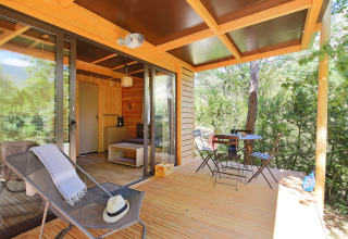 Porche soleado en Victoria Chalet, Camping d'Aix en Provence, Francia, con mesas, sillas y vista al bosque.