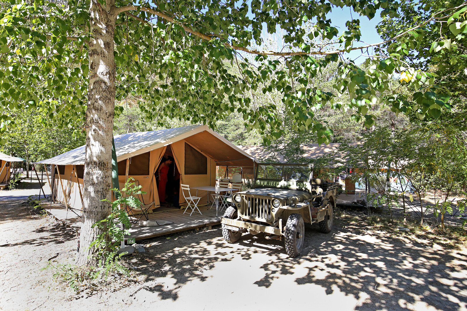 Safari Bungalow tent Classic met terras en jeep onder bomen bij Huttopia Gorges du Verdon in Frankrijk.