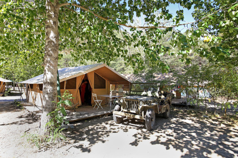 Safari tent Bungalow Classic with terrace and jeep under trees at Huttopia Gorges du Verdon in France.