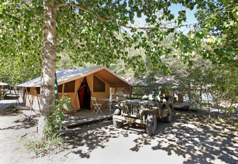 Safari tent Bungalow Classic with terrace and jeep under trees at Huttopia Gorges du Verdon in France.