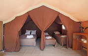 Vista interior de una tienda safari Bungalow tent Classic con tres camas, toallas y zona de cocina.