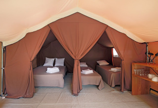 Vista interior de una tienda safari Bungalow tent Classic con tres camas, toallas y zona de cocina.