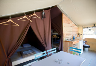 Interno di una tenda safari Toile&Bois Sweet con letto, angolo cucina e tavolo da pranzo.