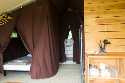Interior de una tienda Toile&Bois tent Sweet en Huttopia Oléron les Pins, Francia, con cama y cocina equipada.