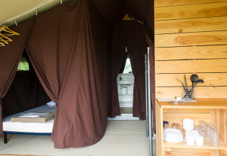 Interior de una tienda Toile&Bois tent Sweet en Huttopia Oléron les Pins, Francia, con cama y cocina equipada.