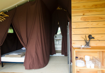 Interior de una tienda Toile&Bois tent Sweet en Huttopia Oléron les Pins, Francia, con cama y cocina equipada.
