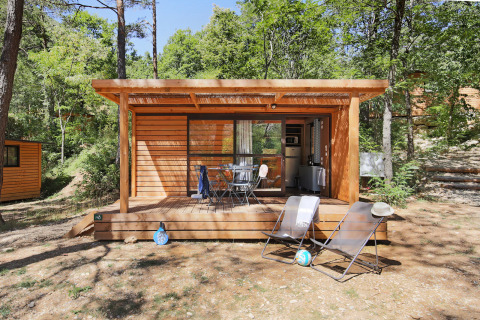 Chalet Evasion houten hut met terras en ligstoelen midden in een rustige, groene bosomgeving.