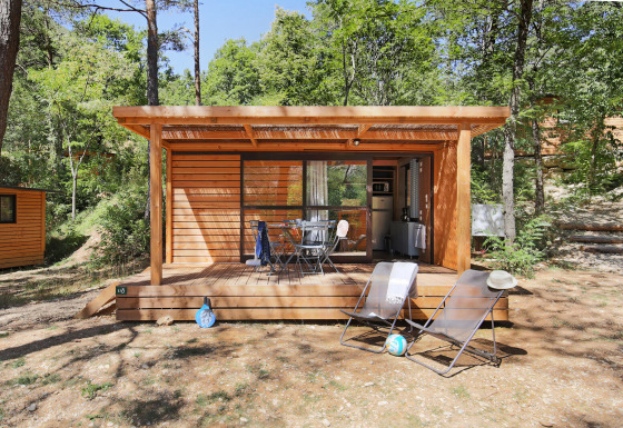 Chalet Evasion houten hut met terras en ligstoelen midden in een rustige, groene bosomgeving.
