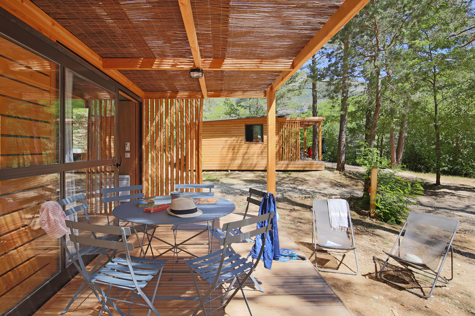 Houten veranda met tafel en stoelen bij Chalet Evasion in Huttopia Gorges du Verdon, omringd door bomen in Frankrijk.
