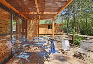 Terraza de madera con mesa y sillas en Chalet Evasion, Huttopia Gorges du Verdon, rodeada de bosque en Francia.