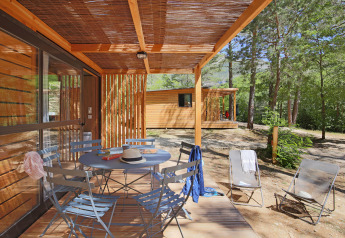 Træveranda med borde og stole på Chalet Evasion ved Huttopia Gorges du Verdon, omgivet af skov i Frankrig.