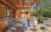 Træveranda med borde og stole på Chalet Evasion ved Huttopia Gorges du Verdon, omgivet af skov i Frankrig.