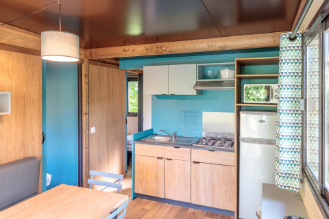 Interieur van Chalet Evasion glampingaccommodatie met keuken, eethoek en zicht op de slaapkamer.
