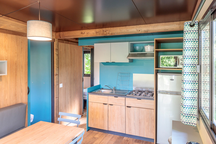 Interior de alojamiento glamping Chalet Evasion con cocina, comedor y vista al dormitorio.