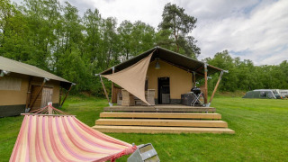 Safaritent bij Wilsumer Berge in Duitsland met hangmat, houten veranda en barbecue in groene natuur.