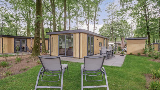 Outdoor photo of Module Wood Hottub lodge with patio furniture and two loungers in a wooded garden.