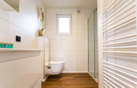 Baño moderno y luminoso en una cabaña, con suelo imitación madera, inodoro suspendido y ducha acristalada.