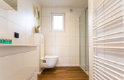 Salle de bain moderne et lumineuse en lodge avec sol effet bois, WC suspendu et cabine de douche vitrée.