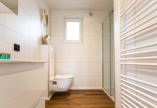Baño moderno y luminoso en una cabaña, con suelo imitación madera, inodoro suspendido y ducha acristalada.