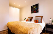 Moderne lodge-slaapkamer met tweepersoonsbed, gouden deken, stijlvolle kussens en kleurrijk kunstwerk.