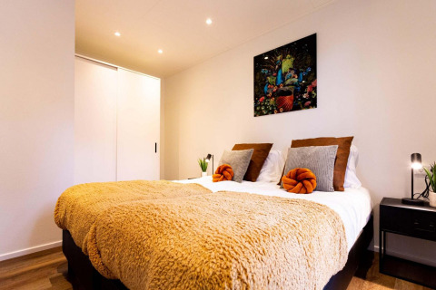 Habitación moderna en lodge con cama doble, manta dorada, cojines elegantes y arte colorido en la pared.