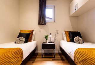 Twin beds with mustard yellow throws and black pillows in Module Wood Hottub at Bospark Ede, Netherlands.