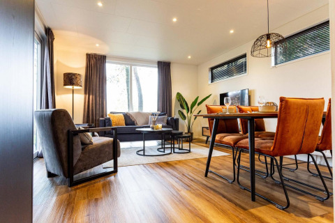 Moderne lodge woonkamer met grote ramen, houten eettafel, oranje stoelen en warme inrichting.