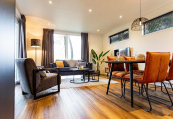 Sala de estar moderna en una cabaña, con ventanas grandes, mesa de madera y sillas naranjas elegantes.