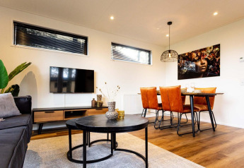 Moderne lodge-stue med sort sofabord, fladskærms-tv, orange spisebordsstole og kunst på væggen.