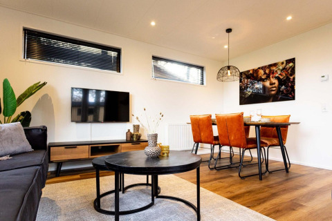 Sala de estar de lodge moderno con mesa de centro negra, TV de pantalla plana, sillas naranjas y arte mural.