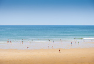 People enjoying the sandy beach and blue waters at Huttopia Lac de Carcans in Nouvelle-Aquitaine, France.