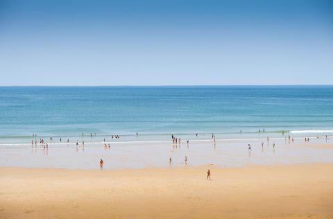 People enjoying the sandy beach and blue waters at Huttopia Lac de Carcans in Nouvelle-Aquitaine, France.