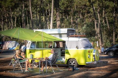 Dos personas acampan junto a una furgoneta retro con toldo en Huttopia Lac de Carcans, Francia.