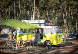 To personer camperer ved en retro varevogn med markise i en skov ved Huttopia Lac de Carcans, Frankrig.