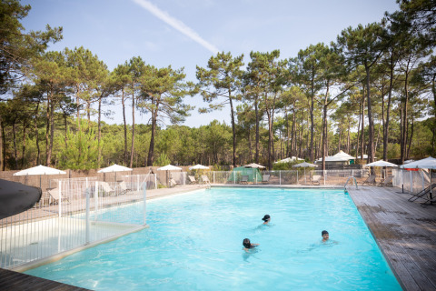 Piscina al aire libre con niños, rodeada de pinos en Huttopia Lac de Carcans, Nouvelle-Aquitaine, Francia.