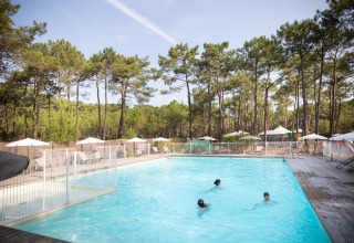 Udendørs swimmingpool med børn, omkranset af skov og liggestole på Huttopia Lac de Carcans i Frankrig.