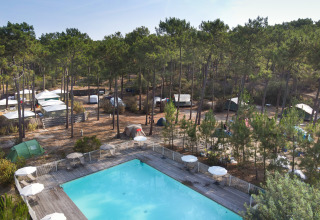 Blick auf Zelte unter Pinienbäumen und einen Außenpool im Huttopia Lac de Carcans, Nouvelle-Aquitaine, Frankreich.