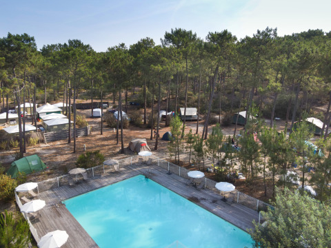 Vue sur des tentes sous les pins et une piscine extérieure à Huttopia Lac de Carcans, Nouvelle-Aquitaine, France.
