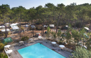 Vista de tiendas entre pinos y piscina exterior en Huttopia Lac de Carcans, Nouvelle-Aquitaine, Francia.