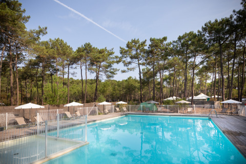 Piscina con tumbonas y sombrillas entre pinos en Huttopia Lac de Carcans, Nouvelle-Aquitaine, Francia.