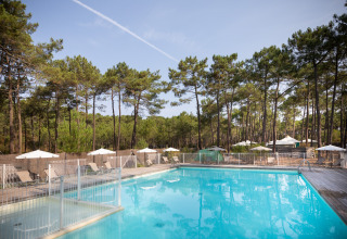 Piscina con tumbonas y sombrillas entre pinos en Huttopia Lac de Carcans, Nouvelle-Aquitaine, Francia.