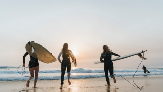Urlauber mit Surfbrettern laufen bei Sonnenuntergang ins Meer im Huttopia Lac de Carcans, Frankreich.