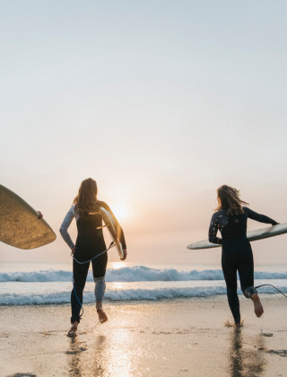Urlauber mit Surfbrettern laufen bei Sonnenuntergang ins Meer im Huttopia Lac de Carcans, Frankreich.